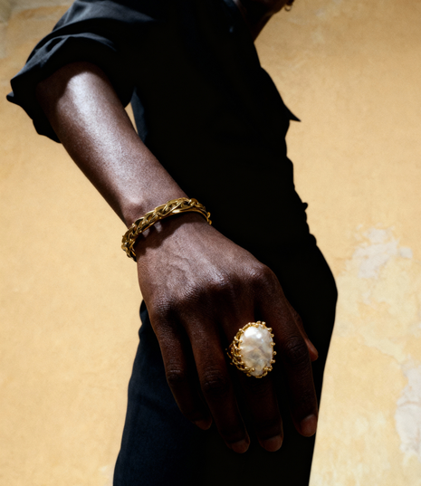 Hand wearing a gold ring and bracelet on a beige background