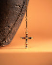 Gold cross earring with colored gemstones on a textured surface