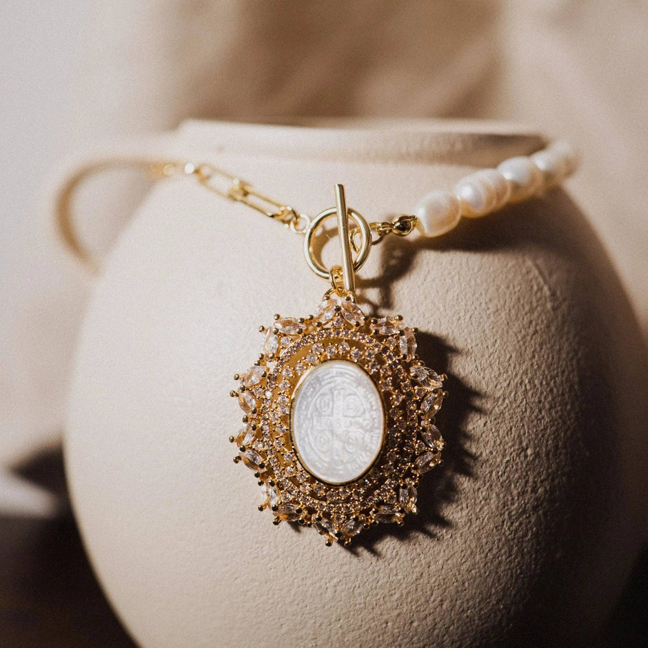 Gold necklace with a pendant on a textured beige surface