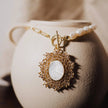 Gold necklace with a pendant on a textured beige surface