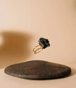 Gold ring with a large black gemstone on a textured beige surface