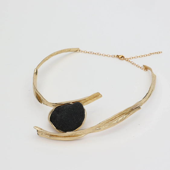 Gold necklace with a black pendant on a light gray background