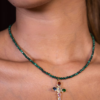 Necklace with a cross pendant featuring green beads and colorful gemstones on a person's neck.