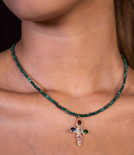 Necklace with a cross pendant featuring green beads and colorful gemstones on a person's neck.