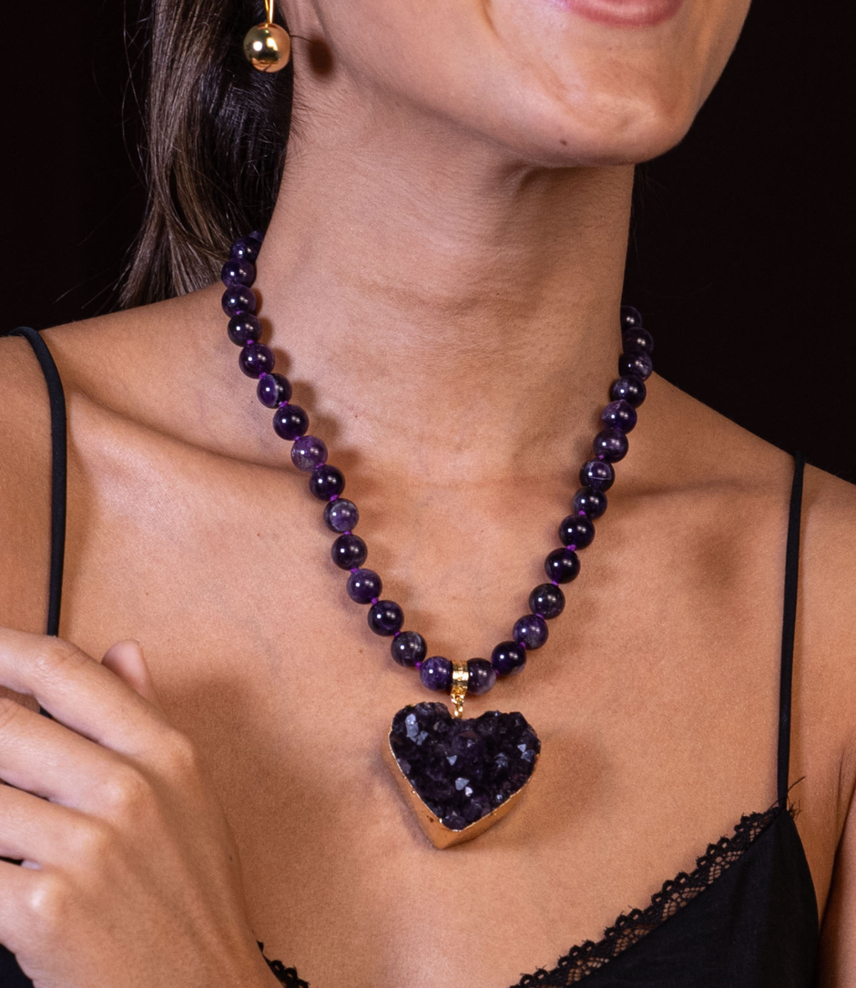 Necklace with a heart-shaped dark purple pendant worn by a person against a black background