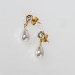 Gold earrings with teardrop-shaped pearls on a light gray background